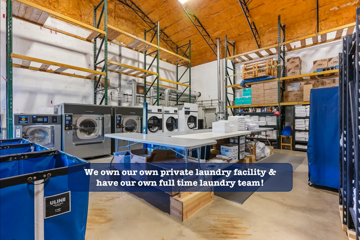 A look inside the dedicated laundry facility, with industrial machines, a table stacked with clean folded linens, and organized storage shelves. The space is immaculately kept, underscoring the property's commitment to cleanliness and professional service.