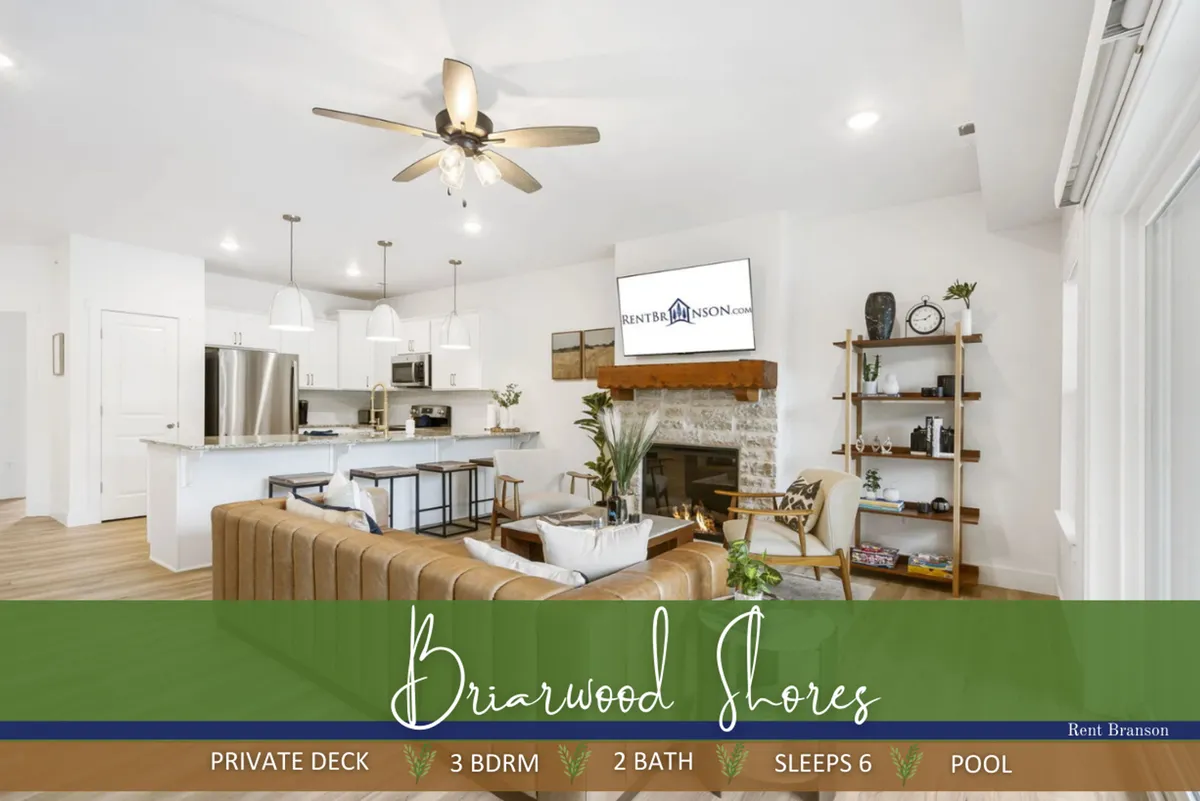 A modern living room with a plush couch, warm fireplace, large television, open kitchen island, and shelving unit. The space is set up for family gatherings with comfortable seating and a cozy, inviting ambiance.