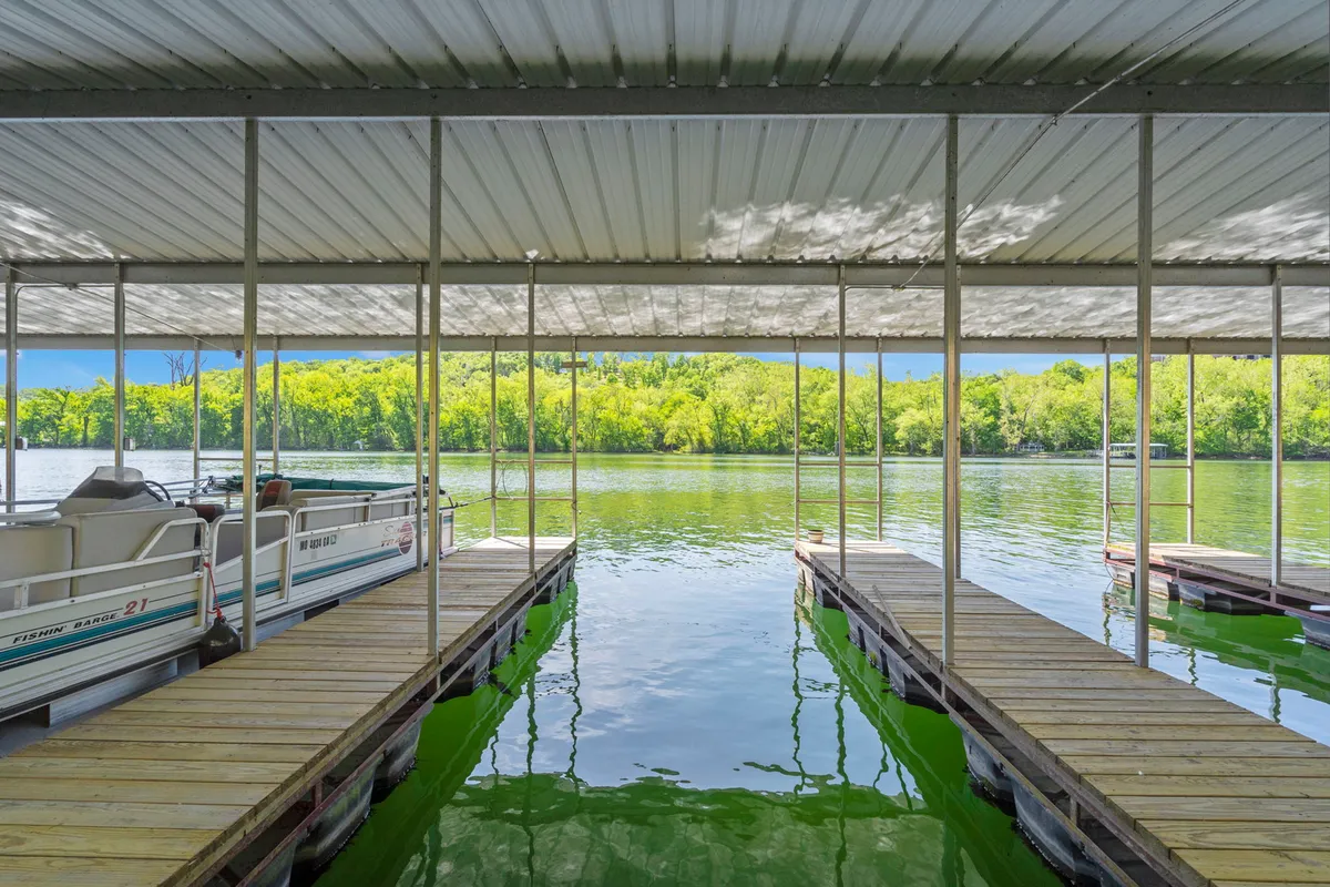 A peaceful dock extends over calm water, surrounded by lush green trees. Boats are moored at the dock, inviting guests to fish, relax, or enjoy nature. The serene mood is perfect for moments of relaxation or casting a line as the sun sets.