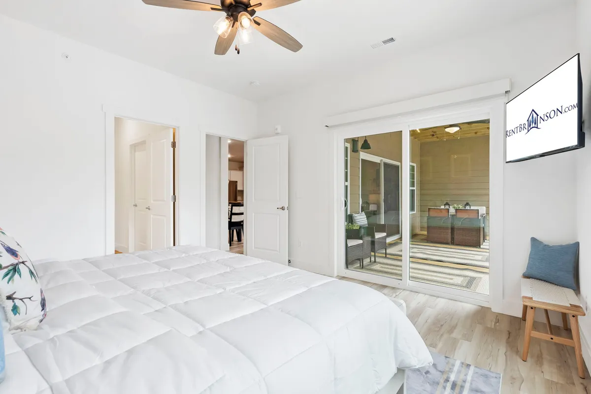 A relaxing King bedroom with a bed facing a sliding door that opens directly to a private patio. The space includes a television and a ceiling fan, creating a calm and cozy area ideal for enjoying the sunrise or stargazing from bed or patio.