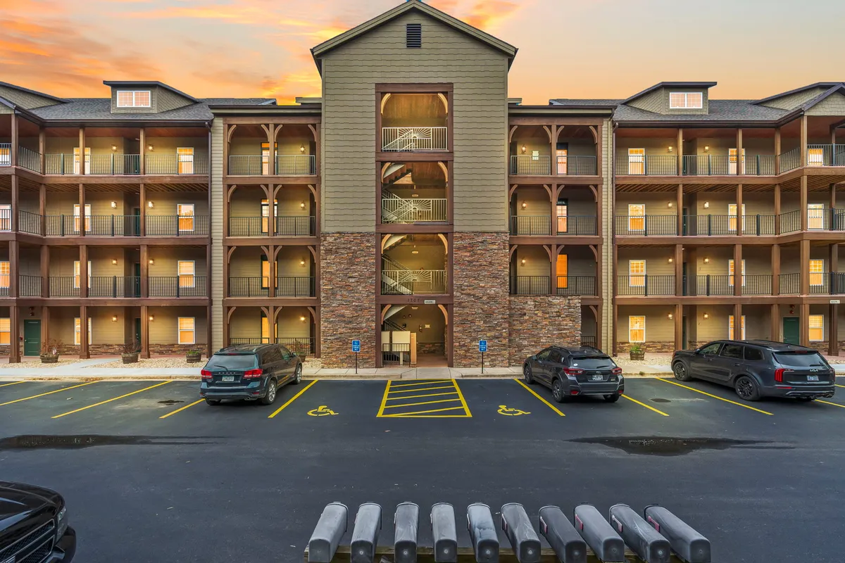 The image captures the main entrance of Briarwood Shores with its staircase, parking area, and exterior architecture. The warm lighting and sunset tones evoke a sense of security and friendly community, reinforcing first impressions.
