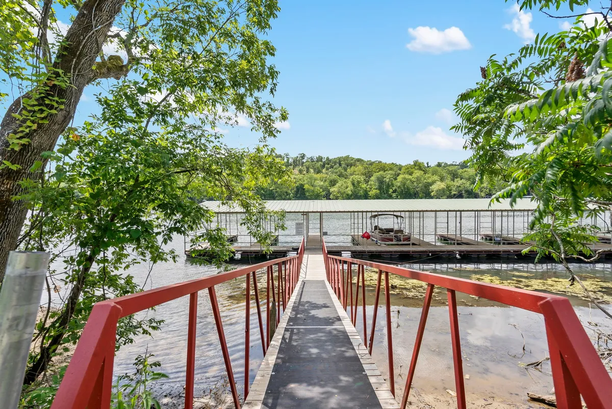 A relaxing exterior view featuring a striking red bridge, a dock leading into calm waters, and trees lining the shore. The setting is perfect for boating, fishing, nature walks, and wildlife observation, evoking the peaceful outdoor adventures available in the area.