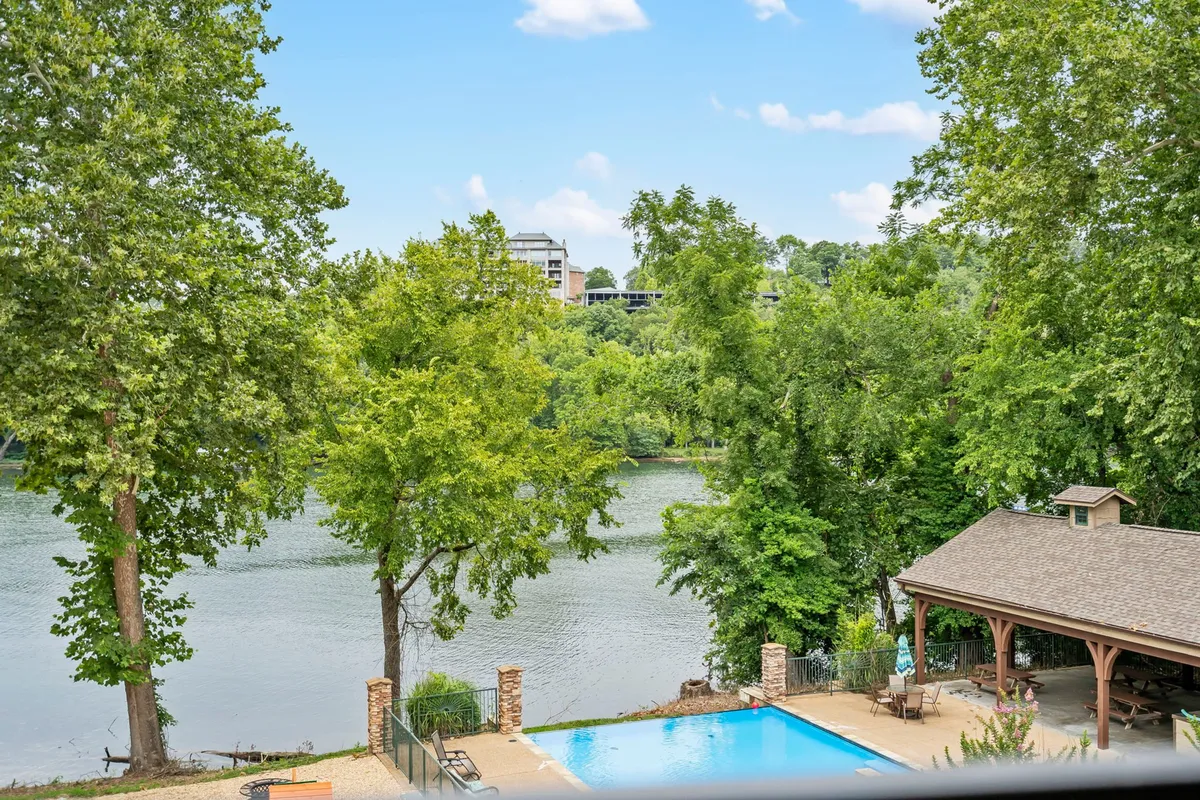 This exterior image showcases a sparkling swimming pool set against the backdrop of a tranquil river and lush trees. Families can be seen enjoying the poolside, with an outdoor pavilion nearby hinting at spaces for gatherings and relaxation. The inviting atmosphere suggests a perfect place for both play and unwinding after a day of adventure.