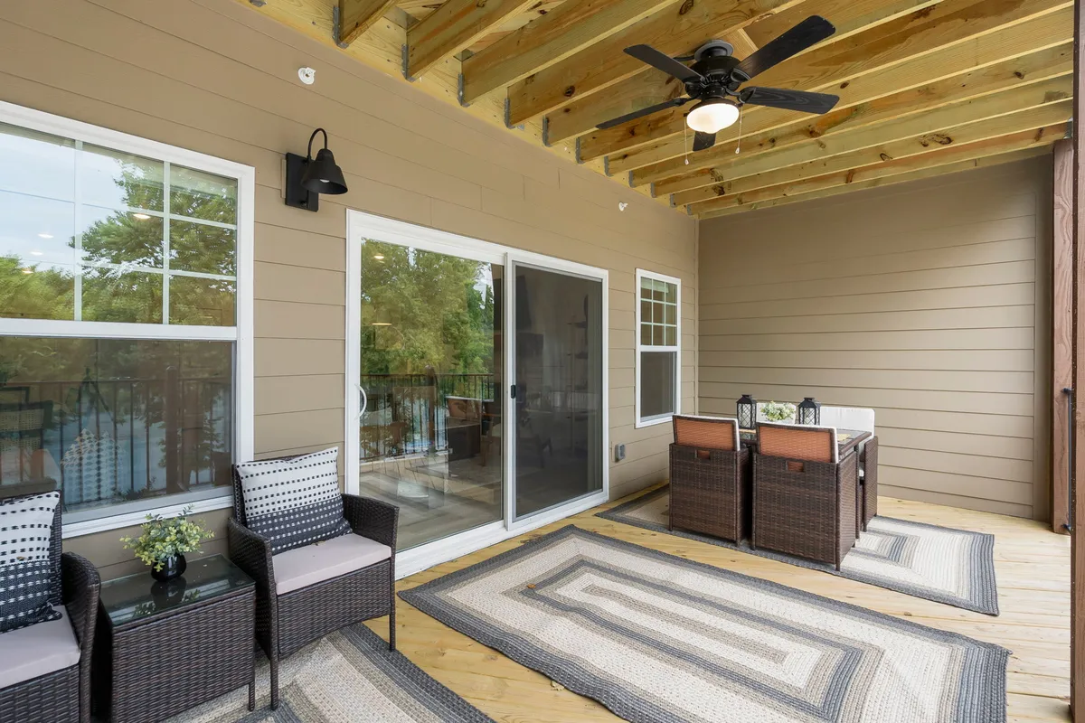 The photo captures a comfortable outdoor seating area on a deck or patio, accented by a decorative rug and ceiling fan. The scene is warmly lit, suggesting pleasant moments spent dining or socializing outdoors with a view of surrounding nature.