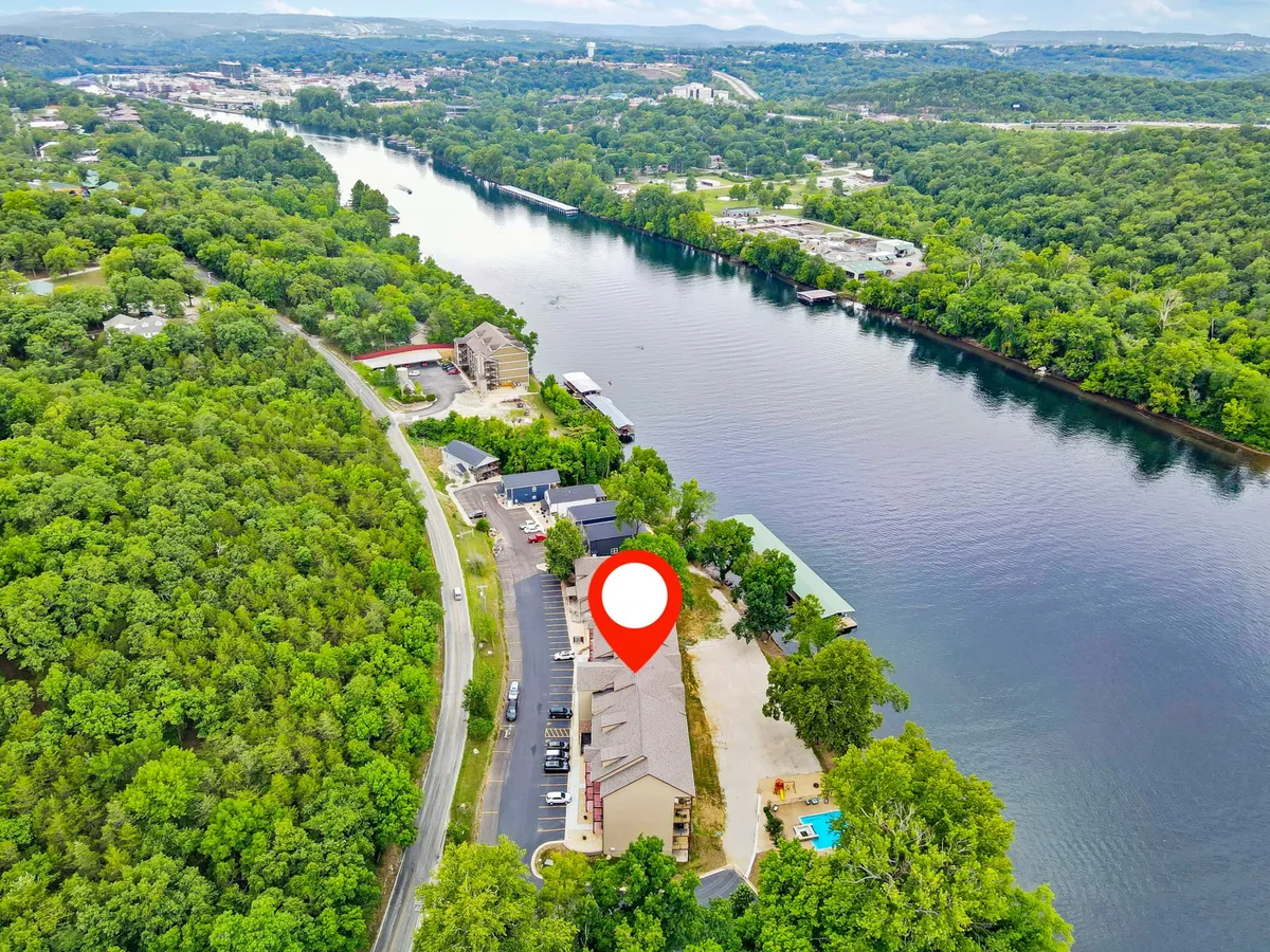 This image presents an exterior view featuring the river, lush greenery, and the building with a pool. The setting suggests outdoor recreation and relaxation, with visible opportunities for activities like boating, fishing, hiking, and enjoying nature near the lodging.